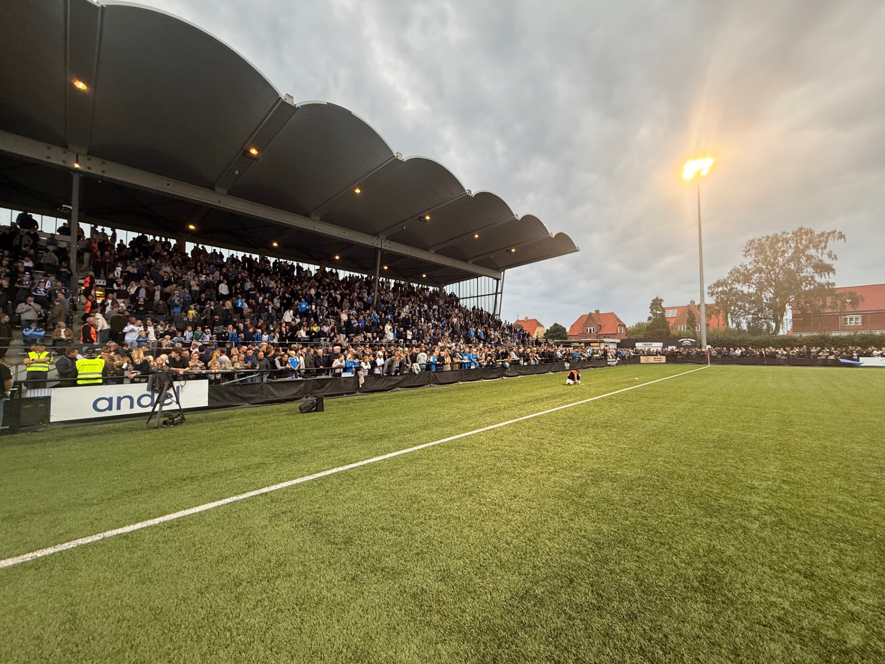 Fyldt tribune på stadion under kampen i aftensolen